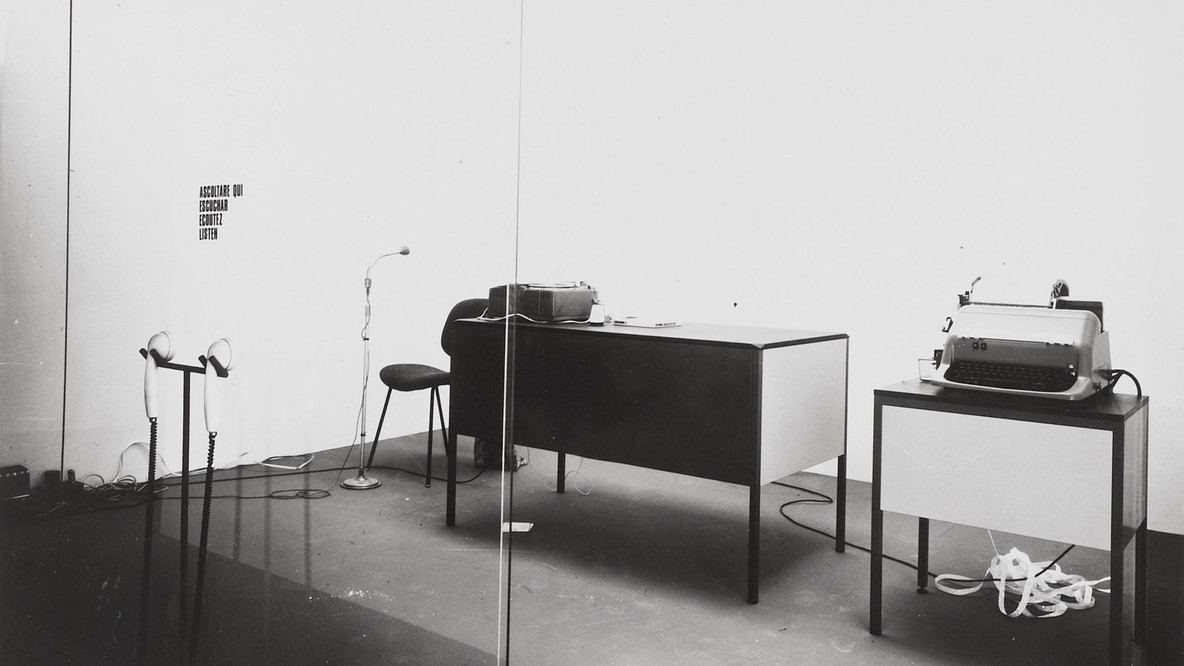 David Lamelas. Office of Information about the Vietnam War at Three Levels: The Visual Image, Text and Audio. 1968. Office furniture, telex machine, tape recorder, microphone, telephone receivers, text, Plexiglas partition, and performance, Dimensions variable. Gift of the artist and Jan Mot, Brussels. © 2024 David Lamelas