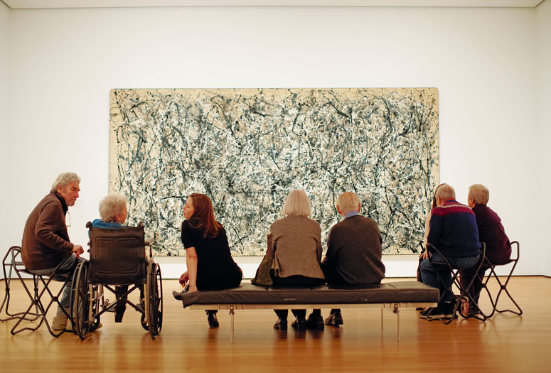 Photo: Jason Brownrigg. Digital image © 2024 The Museum of Modern ArtImage description: Eight adults seated, facing Jackson Pollock’s One: Number 31, a wall-filling beige canvas scattered with dark gray, white, blue, and tan drips that erratically swing in abstract movement.