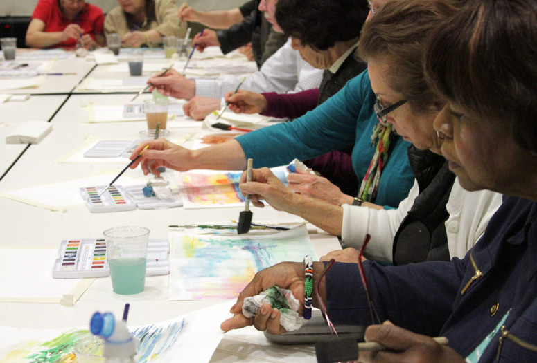 Photo: Manuel Molina MartagonImage description: Profile view of a long table of older adults painting with watercolors
