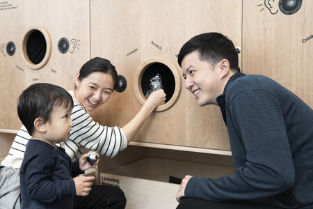 Photo: Martin SeckImage description: Parents and young child listing to the sounds materials make at the Listening Wall in Art Lab: Sound.