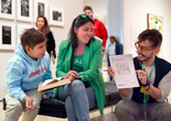 Photo: On White WallImage description: A caregiver and child look on as a smiling educator holds up a worksheet.