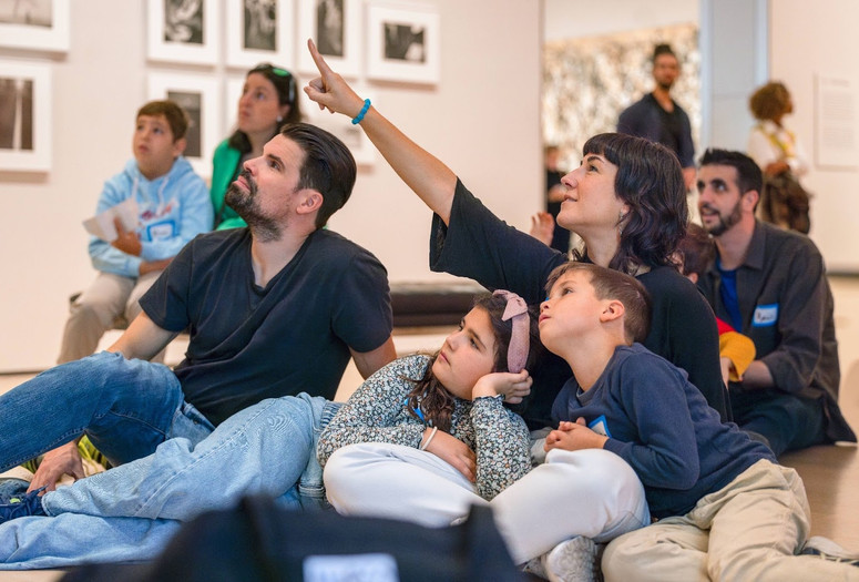Photo: On White WallImage description: A caregiver points to an artwork while the rest of the family observes.