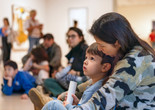 Photo: On White Wall Inc.Image description: A child sits on their caregiver’s lap on the floor of the Museum galleries while gazing up at artwork.