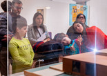 Photo: On White Wall, Inc.Image description: An educator and families view a work displayed behind glass together.
