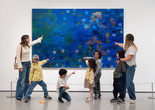 Photo: On White Wall Inc.Image description: A group of families point and pose in front of an artwork.