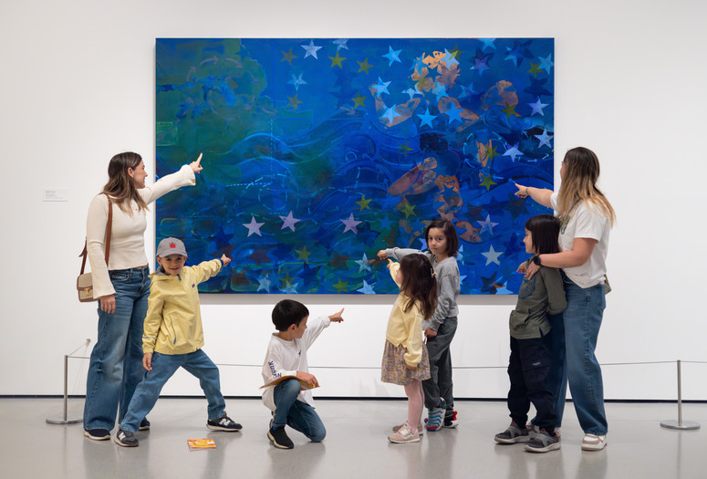 Photo: On White Wall Inc.Image description: A group of families point and pose in front of an artwork.