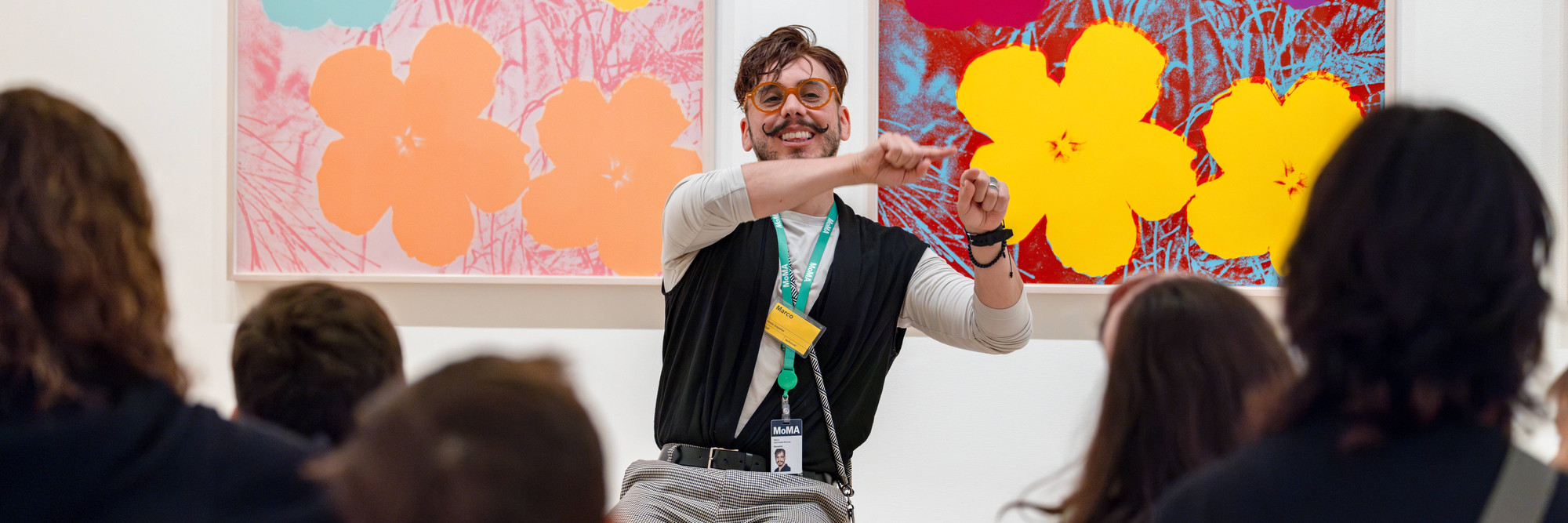 A smiling educator explains two works of art to seated families. Photo: On White Wall Inc.