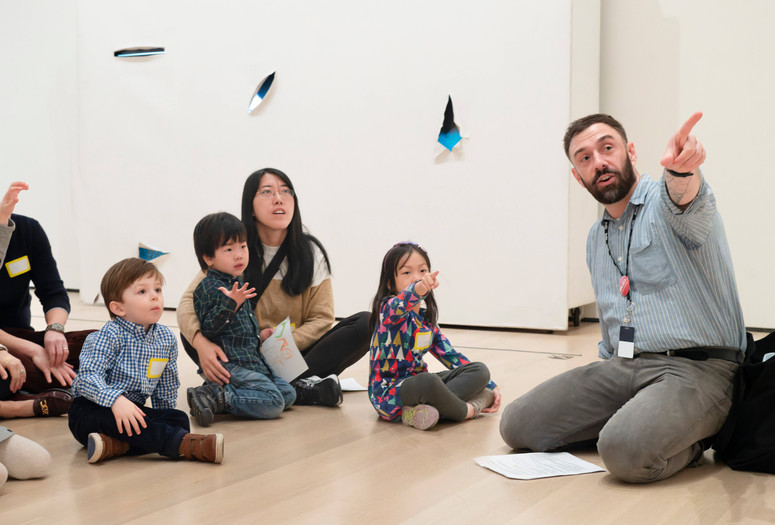 Photo: Martin SeckImage description: An educator points at an artwork while families with young children observe.