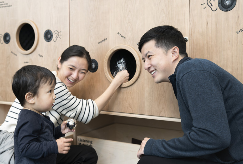 Photo: Martin SeckImage description: Parents and young child listing to the sounds materials make at the Listening Wall in Art Lab: Sound.