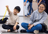 Photo: On White Wall Inc.Image description: A child dangles a yellow string of model magic as he sits on the floor with a caregiver.