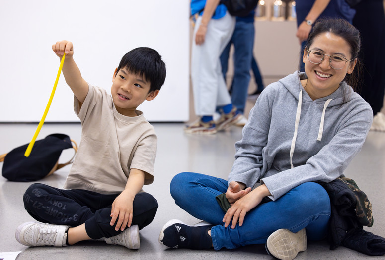 Photo: On White Wall Inc.Image description: A child dangles a yellow string of model magic as he sits on the floor with a caregiver.