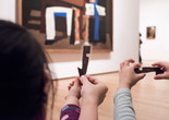 Photo: Martin SeckImage description: Children hold up laminated paper cutouts in front of an artwork.
