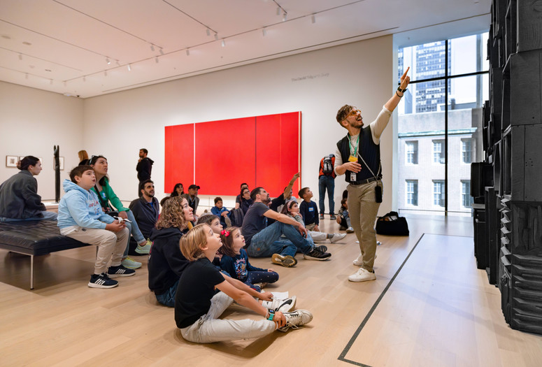 Photo: On White Wall Inc.Image description: An educator points at an artwork and leads a group of families in a discussion.