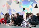 Photo: Martin SeckImage description: A tween points upwards with a pencil while other tweens draw on the gallery floor.