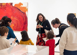 An educator leads a gallery talk for a group of families in front of a bright red painting. Photo: On White Wall Inc.