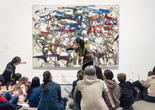 An educator points at streaks of paint in front of an artwork as families observe. Photo: On White Wall Inc.