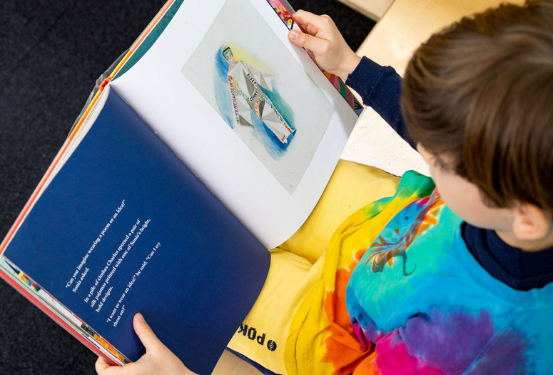 A child looks down at a picture book on his lap. Image courtesy On White Wall, Inc.
