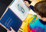 A child looks down at a picture book on his lap. Image courtesy On White Wall, Inc.