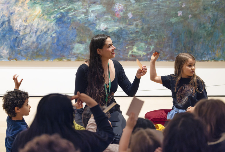 An educator leads a discussion in front of an artwork as two young children raise their hands. Photo: On White Wall, Inc.