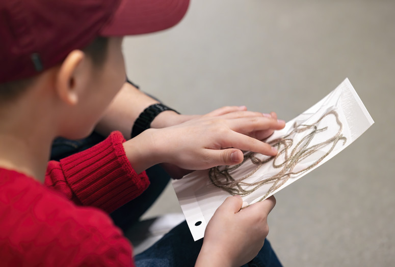A child holds their composition of brown string on a white sticky board Photo: On White Wall Inc.