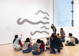 An educator leads a discussion with families in front of an artwork with large, cut-out, squiggly lines. Photo: On White Wall