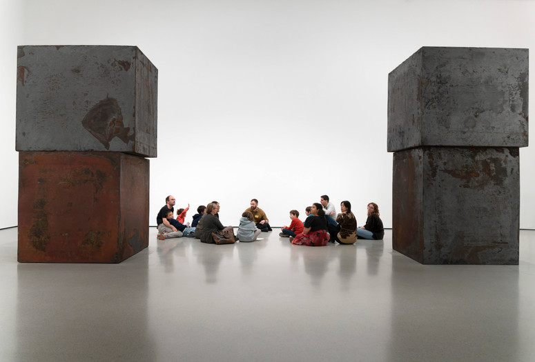 A group of families sit in a gallery featuring Richard Serra’s large sculpture Equal. Photo: Martin Seck
