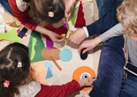 A group of four family members, photographed from above, add felt shapes of different colors to a background. Photo: On White Wall, Inc.