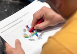 A closeup of a hand drawing on an activity sheet featuring a circle with colorfully drawn shapes inside. Photo: On White Wall Inc.