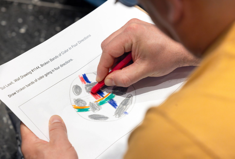 A closeup of a hand drawing on an activity sheet featuring a circle with colorfully drawn shapes inside. Photo: On White Wall Inc.