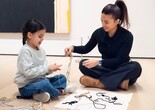 A child and an adult sit on the floor in the galleries arranging a composition with string. Photo: On White Wall, Inc.