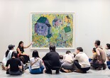 An educator leads a conversation with a group of young children and their families in front of an artwork depicting houses of different colors. Photo: On White Wall Inc.