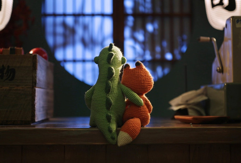 Lost and Found. 2018. Australia. Directed by Andrew Goldsmith, Bradley Slabe. Image courtesy Gerald Thompson. Image description: A knitted dinosaur and fox sit together on a counter, the dinosaur’s arm around the fox, gazing at a softly lit, round window.