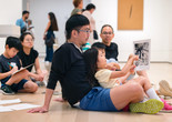 During a gallery talk, a child sits in their adult’s lap and points to an image of the artist Jackson Pollock splattering paint. Photo: On White Wall, Inc.