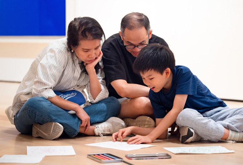 A child and two adults do a drawing activity on the floor during Family Art Adventures in Mandarin. Photo: On White Wall, Inc.