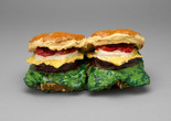 Claes Oldenburg. Two Cheeseburgers, with Everything (Dual Hamburgers). 1962. Burlap soaked in plaster, painted with enamel. The Museum of Modern Art, New York. Philip Johnson Fund. © 2025 Claes Oldenburg Image description: Colorful sculpture of two burgers with layers of red, yellow, green, and brown. The predominant colors are tan for the buns and vibrant greens, yellows, and reds for fillings.
