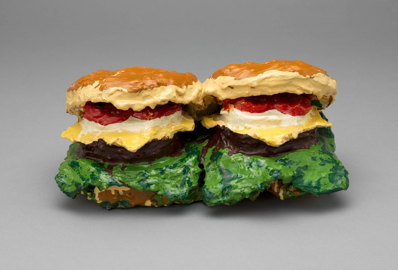 Claes Oldenburg. Two Cheeseburgers, with Everything (Dual Hamburgers). 1962. Burlap soaked in plaster, painted with enamel. The Museum of Modern Art, New York. Philip Johnson Fund. © 2025 Claes Oldenburg Image description: Colorful sculpture of two burgers with layers of red, yellow, green, and brown. The predominant colors are tan for the buns and vibrant greens, yellows, and reds for fillings.
