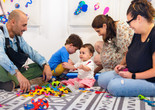 Young children and adults sit on a patterned mat, looking at one another and playing with colorful shapes. Photo: On White Wall, Inc.