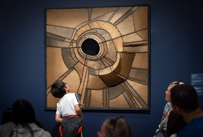 During a Family Gallery Talk, a child examines an artwork made of many pieces of brown fabric with a hole in the center. Artwork: Lee Bontecou. Untitled. 1959. Welded steel, canvas, black fabric, soot, and wire. The Museum of Modern Art, New York. Gift of Mr. and Mrs. Arnold H. Maremont. © 2026 Lee Bontecou. Photo: On White Wall, Inc.
