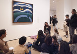 An educator kneels in front of a work of art and leads a discussion about the artwork with a group of families. Photo: On White Wall, Inc.