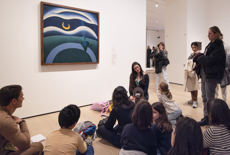 An educator kneels in front of a work of art and leads a discussion about the artwork with a group of families. Photo: On White Wall, Inc.