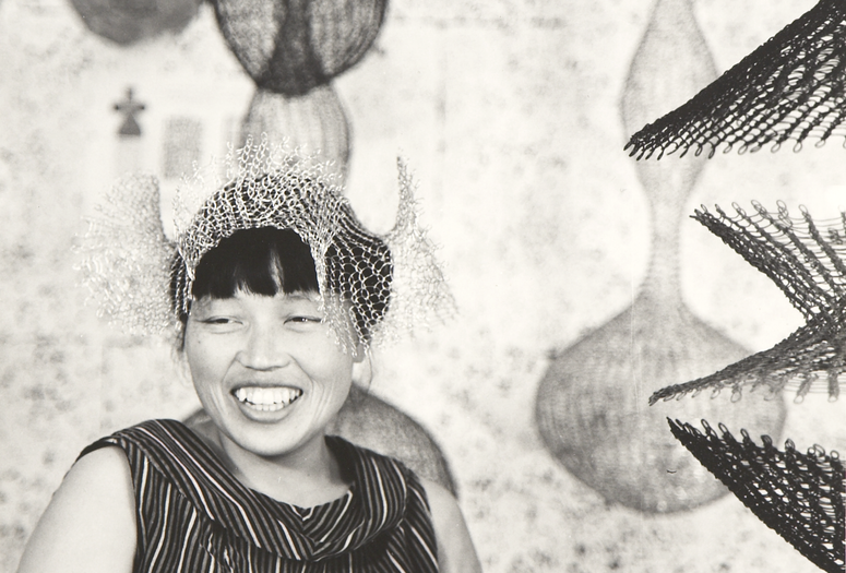 Ruth Asawa wearing a looped-wire crown amongst other sculptures, 1958. Photo © Estate of Paul Hassel. Artwork © 2026 Ruth Asawa Lanier, Inc., Courtesy David Zwirner