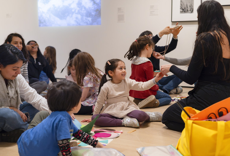 A child sits among other families in the galleries and passes a material to an educator. Photo: On White Wall, Inc.