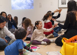 A child sits among other families in the galleries and passes a material to an educator. Photo: On White Wall, Inc.