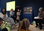 An educator leads a discussion with families in front of a sculpture of a pastry case with sculpted desserts inside. Photo: On White Wall, Inc.
