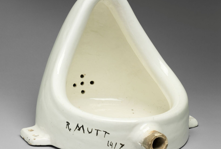Marcel Duchamp. Fountain. 1950 (replica of 1917 original). Porcelain urinal. Philadelphia Art Museum: 125th Anniversary Acquisition. Gift (by exchange) of Mrs. Herbert Cameron Morris. © Association Marcel Duchamp/ADAGP, Paris/Artists Rights Society (ARS), New York 2026 Image description: A white porcelain urinal turned 90 degrees so it sits on the flat side that would have been flush against the wall. The words “R. Mutt 1917” are written in thick black paint on the rim of the base.