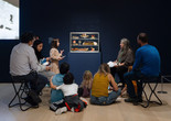 An educator leads a discussion with families in front of a sculpture of a pastry case with sculpted desserts inside. Photo: On White Wall, Inc.