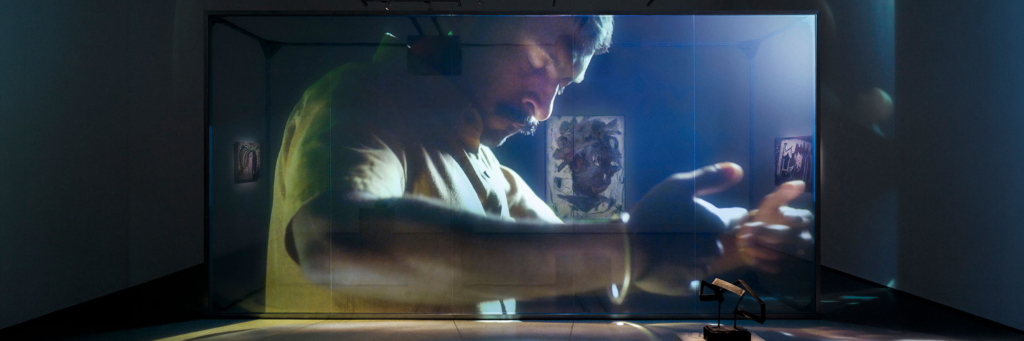 Christopher Kulendran Thomas. Being Human. 2019. High-definition video (color, sound; 24 min.) projected on glass, with three paintings and three sculptures: Untitled II, Untitled V, and Untitled VI (2018) by Upali Ananda, and Untitled II and Untitled V (2018) by Kingsley Gunatillake (all purchased by the artist from Saskia Fernando Gallery, Colombo); and Untitled X after Kingsley Gunatillake (2019) by Christopher Kulendran Thomas. In collaboration with Annika Kuhlmann. The Museum of Modern Art, New York. Acquired through the generosity of Charles Asprey and Markus Hannebauer, 2021. © Christopher Kuelndran Thomas