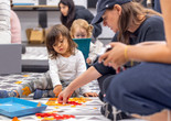 A caregiver and two children work together with orange tissue paper to make a collage. Courtesy: On White Wall, Inc.