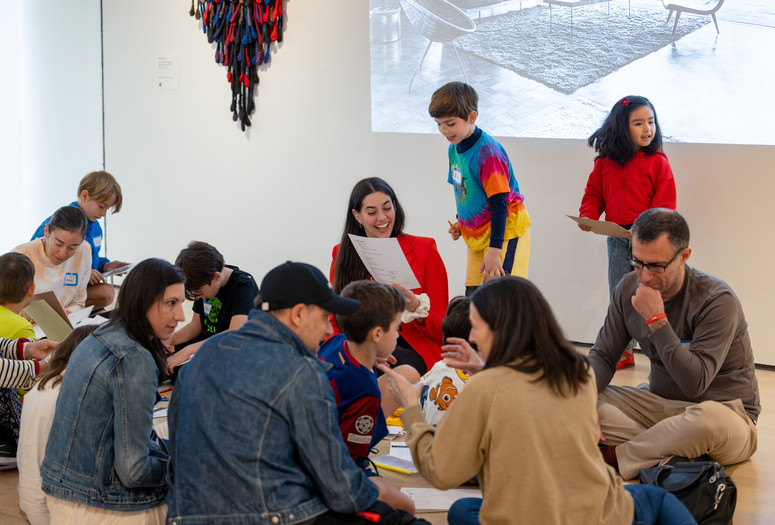 An educator smiles at a child in the galleries while looking at the child’s artwork. Photo: On White Wall, Inc.