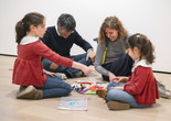 A family sits on the floor of the gallery and works on a collage with brightly colored felt shapes. Photo: On White Wall, Inc.
